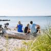 Familie sidder på stranden og kigger ud over vandet med cykler ved siden af