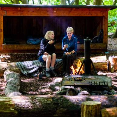 To kvinder ved bål foran shelter i Kollund Skov