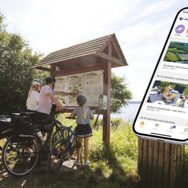 En familie står og kigger på et kort, og der er en mockup af en mobil med en åben app.