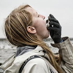 Pige i regnjakke spiser frisk østers i Vadehavet