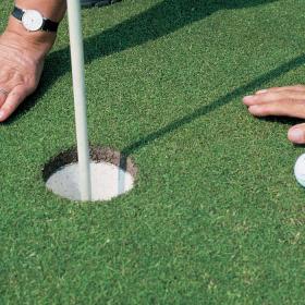 To hænder med golfbolde ved et hul på en golfbane